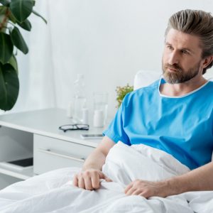 patient in medical gown sitting on bed and looking away in hospital