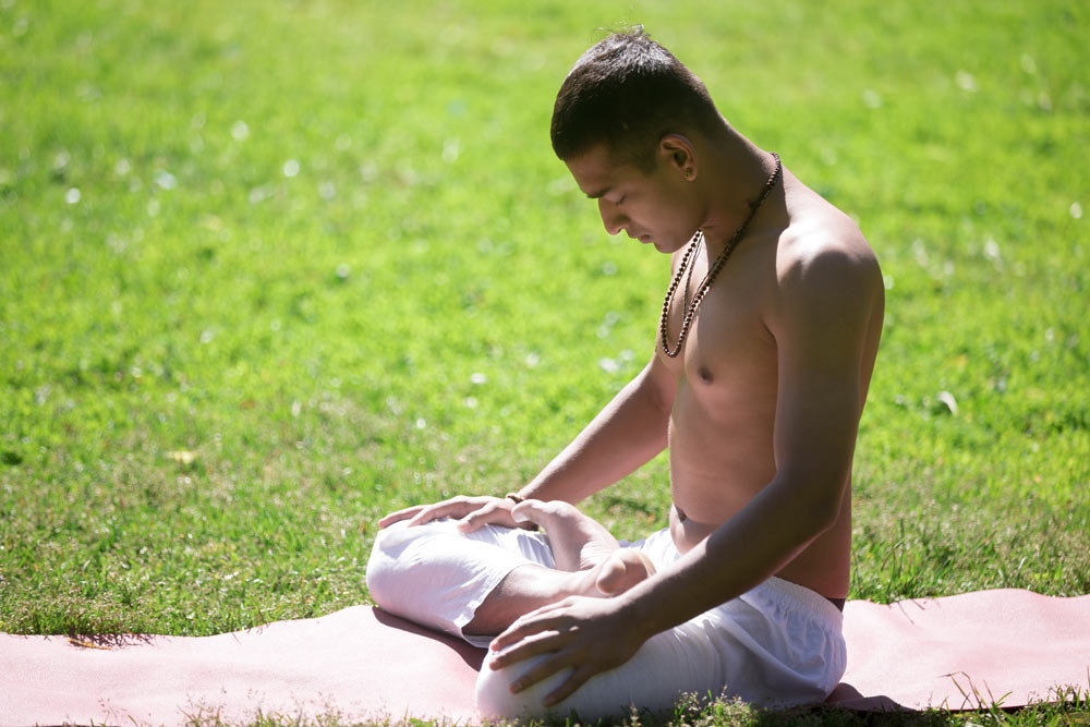 Serene man practicing yoga on green grass